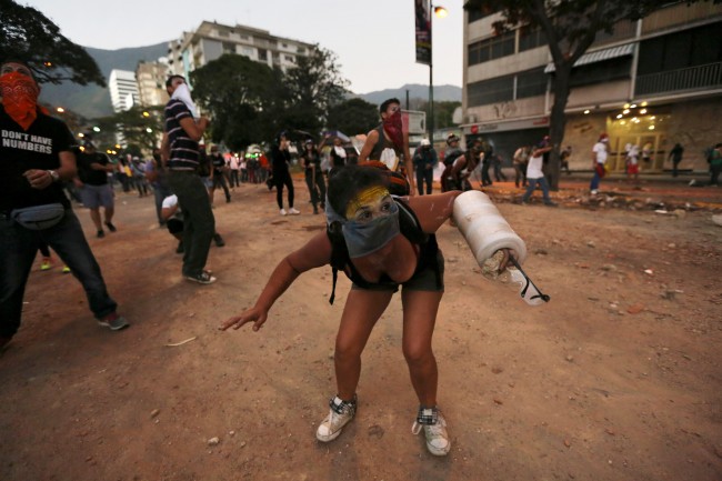 A demonstrator using foam to protect her arm ducks from team gas fired by Bolivarian National Police during clashes in Caracas, Venezuela, Monday, March 3, 2014. Venezuelan opposition leader Henrique Capriles called for citizens to begin organizing committees that could sustain the pressure that continuing street protests have placed on the government of President Nicolas Maduro.