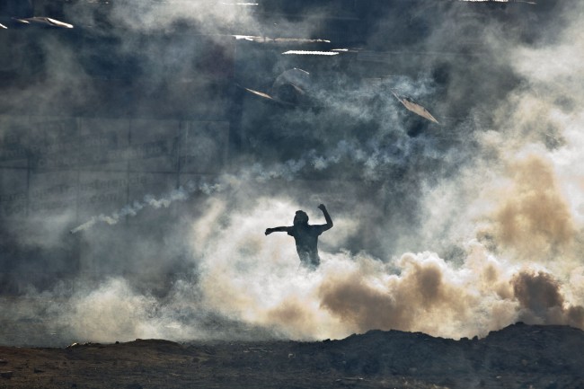 An anti-government demonstrator standing in teargas fired by Bolivarian National Guards prepares to throw a rock during clashes near Plaza Altamira in Caracas, Venezuela, Sunday, March 16, 2014.