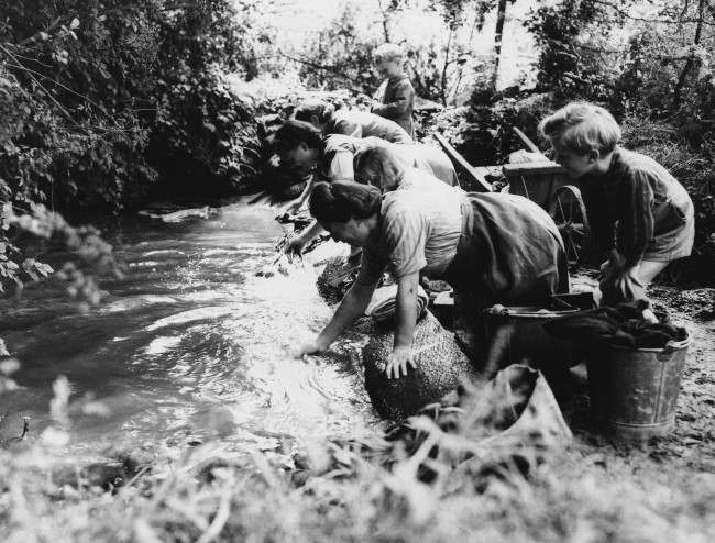 French children watch their mothers wash clothes in a brook in Normandy on August 23, 1944 in an area liberated from the Nazis by American Forces. (AP Photo/Lawrence Riordan)