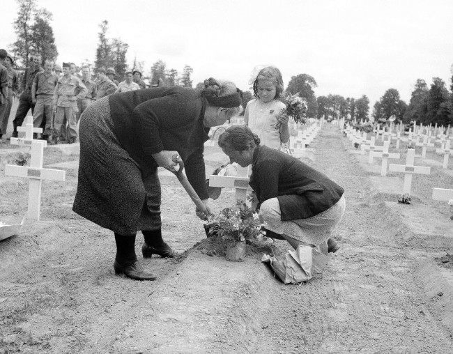 A French family living in the La Cambe area of Normandy, France on July 15, 1944, now liberated by the allies, place flowers on the graves of the U.S. dead as part of the Bastille Day celebrations. (AP Photo/Bede Irvin)