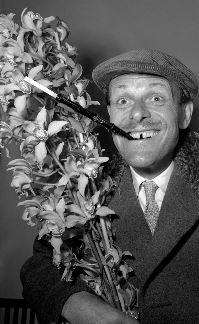TV's elegant comedian Terry-Thomas, who exhibits a distinctive sartorial style, returns from a holiday in Madeira sporting a cap and extended cigarette holder. He carries a bush of orchids for his wife. PA/PA Archive/Press Association Images
